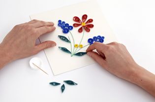 hands shaping a quilled design on a sheet of paper