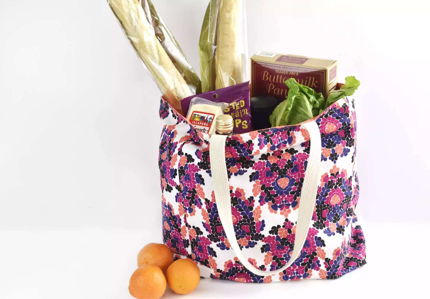 A purple floral reusable grocery bag filled with groceries