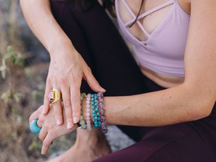 女性的手互相抚摸着，戴着几枚由宝石制成的戒指和手镯，穿着瑜伽裤