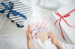 female hand holding gift box with gift tag on the bed