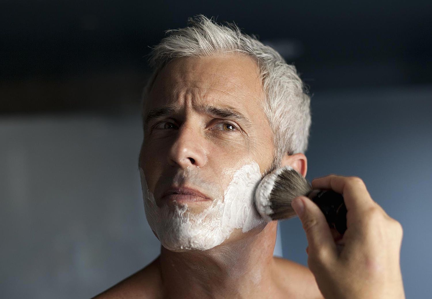 成熟的男人在剃须前在脸上打泡沫