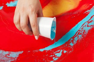 如何制作丙烯画。工作正在进行中。女性手拿一个涂有蓝色油漆的塑料杯。