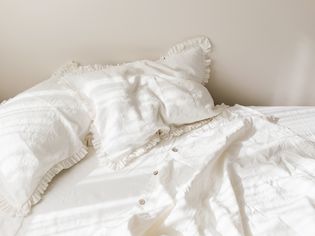 空白色亚麻床上用品与褶边枕头在早晨闪耀的阳光。
