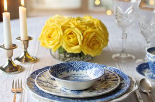 Place setting with vintage dinnerware, arrangement of yellow flowers, and lit candles..