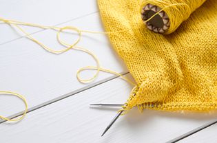 羊毛衫一种用棉制成的未捆绑的轻便夏季毛衣或开衫旁边是一束纱线和编织针，背景是一张白色的木桌。自由创作的工作和生活理念，爱好。