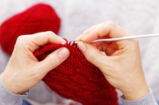 Closeup womans hands knitting red burgundy wool yarn