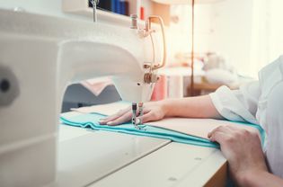 缝纫机和女性的手特写。年轻的裁缝在设计工作室用布料缝纫和工作。小型企业