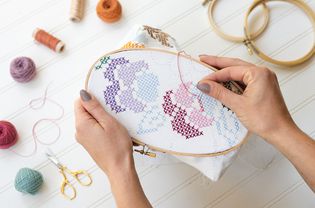 Cross-stitch pattern being sowed with purple, blue and pink thread