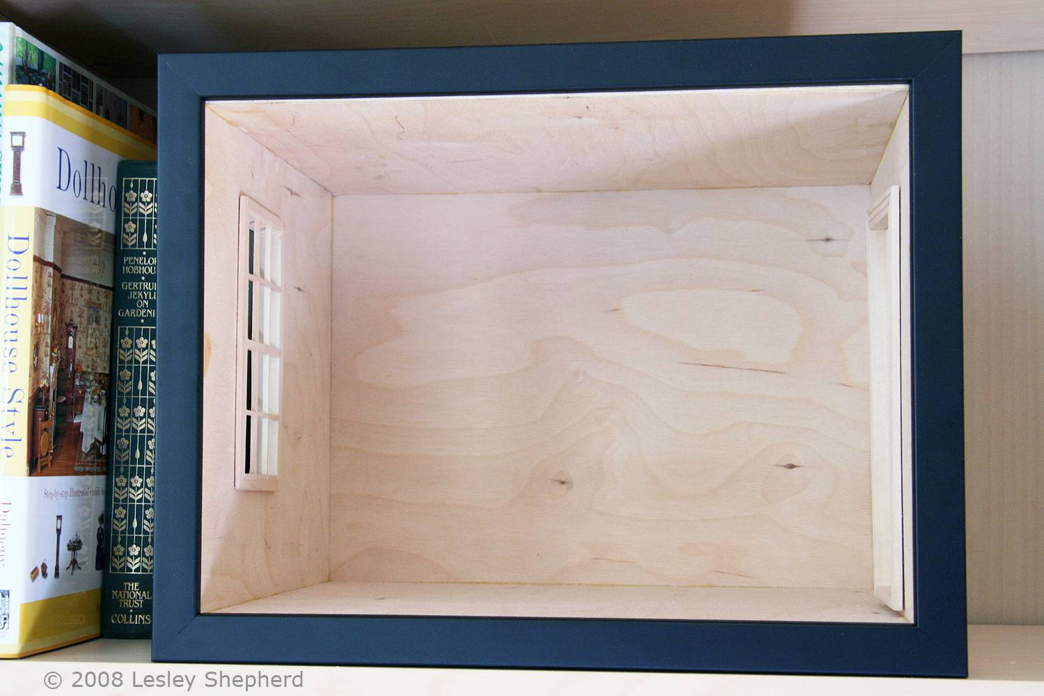 一个简单的画框包围了一个娃娃屋比例房间盒子的前部，它可以放在书架上。