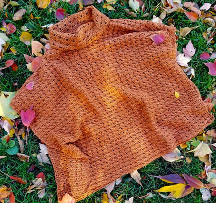 Orange poncho laying on a lawn with colorful leaves