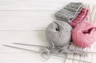 Grey and pink knitting wool and knitting needles on white wooden background.