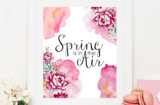 A spring printable framed on a table by flowers and cookies.