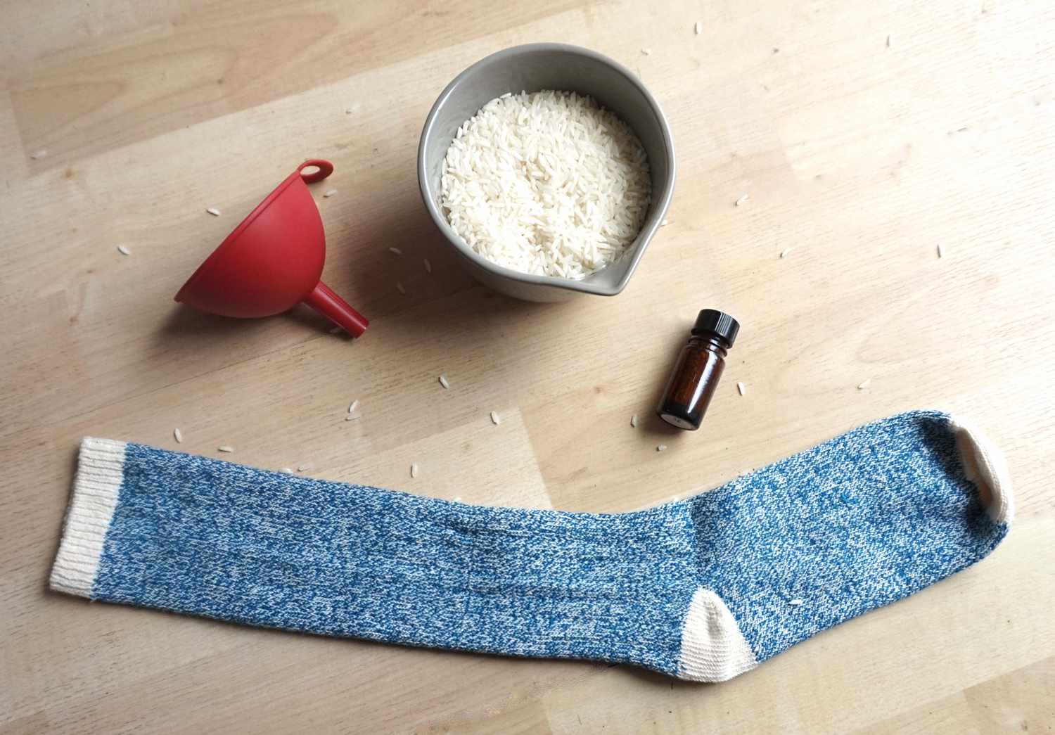 一碗米饭,一个红色的塑料漏斗,一瓶精油和蓝色针织袜子木背景。