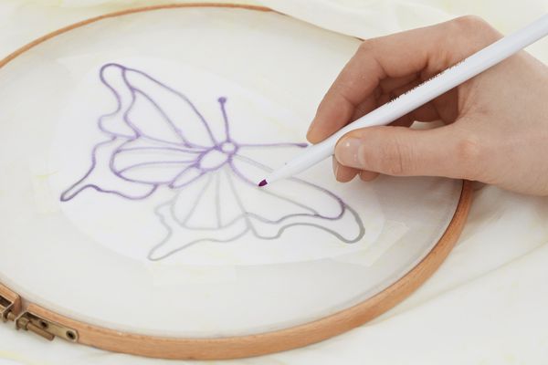 Tracing over lines of butterfly motif on silk scarf secured to embroidery hoop.