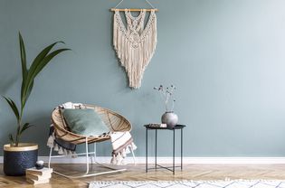Stylish minimalistic interior of living room with design rattan armchair, black coffee table, tropical platn in basket, beige macrame on the wall and elegant accessories. Eucalyptus color of wall.
